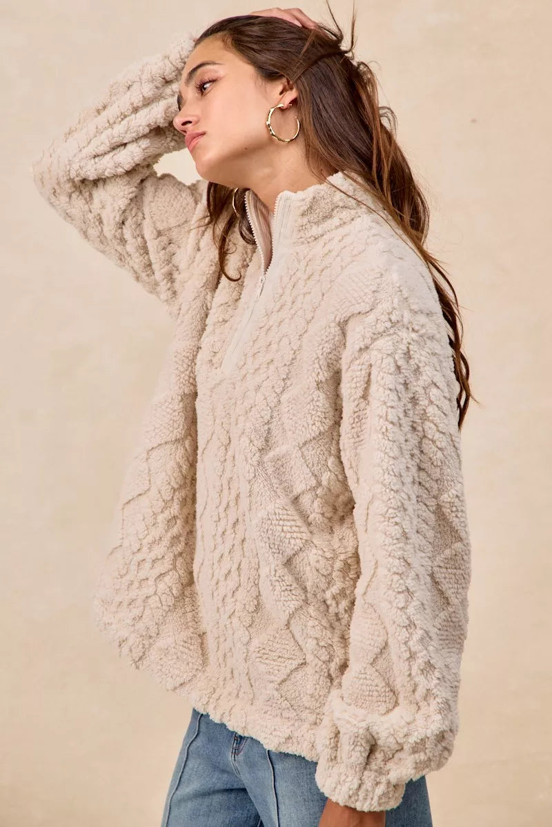 Model wearing the Vanilla Frost Cable Fleece Pullover — a cream-colored, cable-textured fleece half-zip sweater with a relaxed, cozy fit.