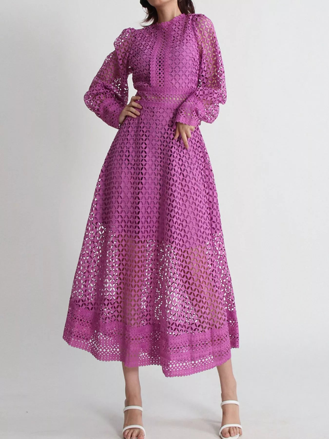 Model wearing the Violet Lace Cutout Midi Dress with long sheer balloon sleeves, high neckline, and geometric lace design, styled with white strappy heels.