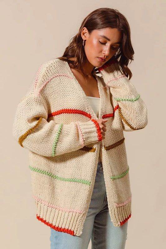 Woman wearing an oversized cream cardigan with multicolor stripe accents — cozy open knit sweater from A Whimsical Affair.
