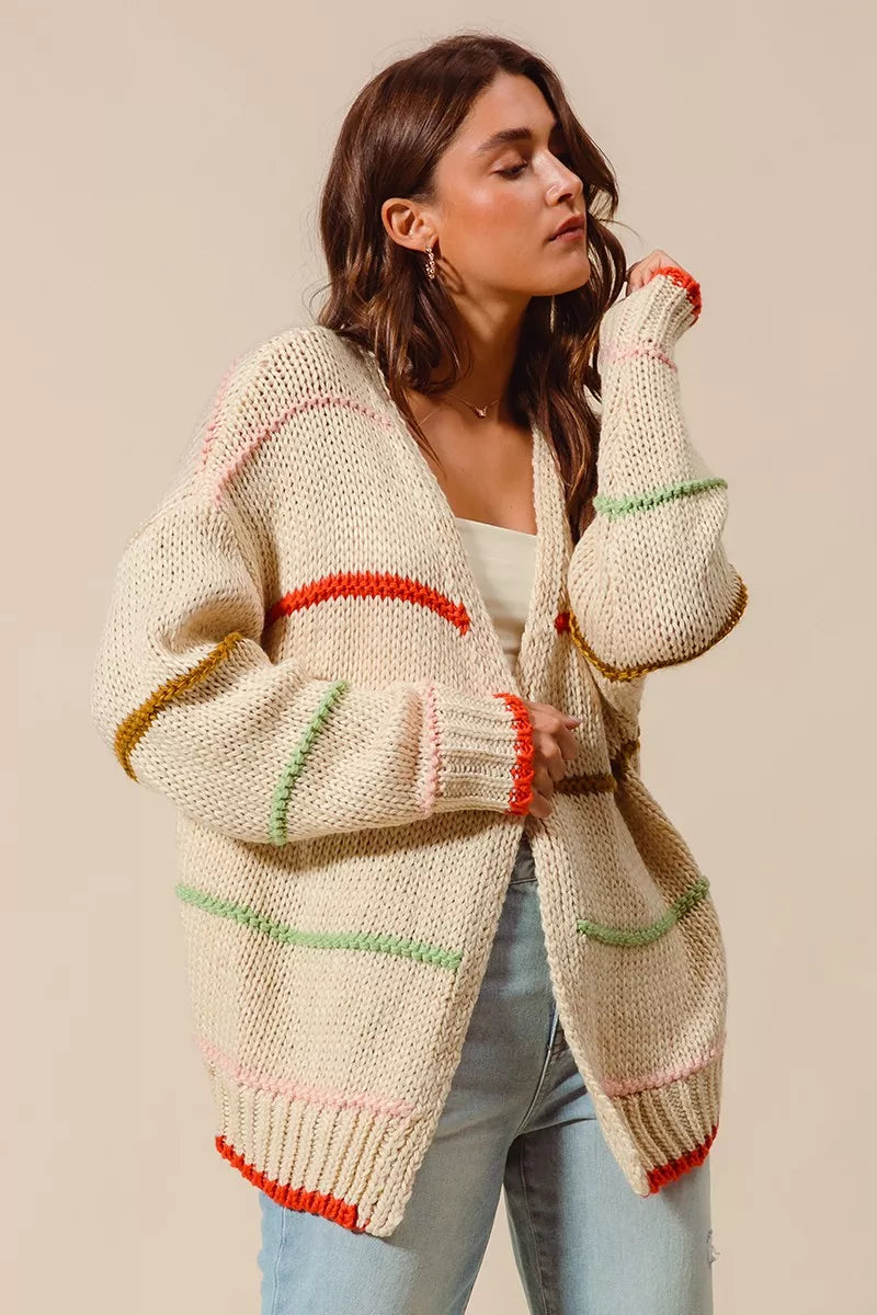 Woman wearing an oversized cream cardigan with multicolor stripe accents — cozy open knit sweater from A Whimsical Affair.