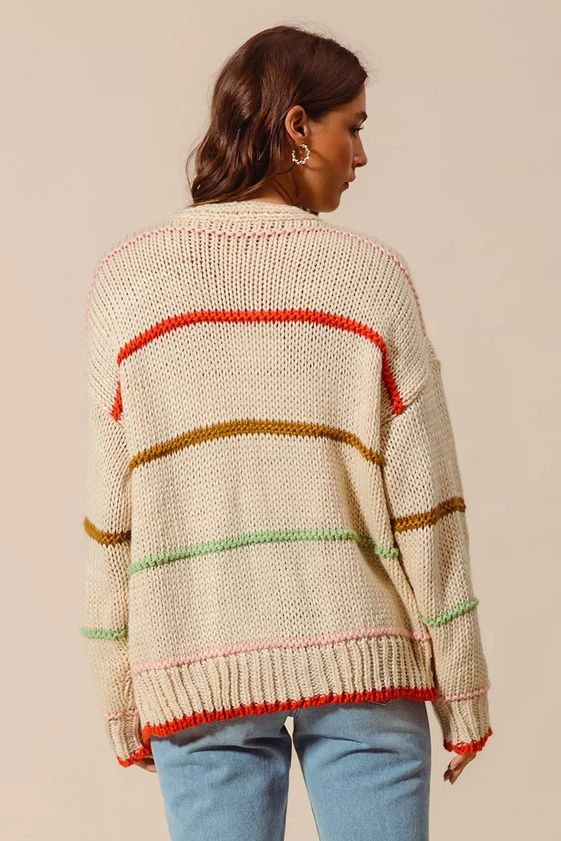 Woman wearing an oversized cream cardigan with multicolor stripe accents — cozy open knit sweater from A Whimsical Affair.
