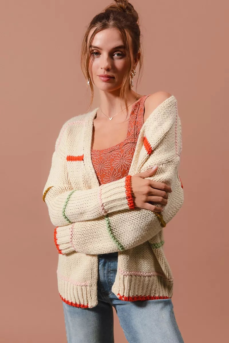 Woman wearing an oversized cream cardigan with multicolor stripe accents — cozy open knit sweater from A Whimsical Affair.