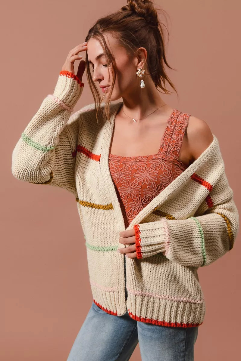 Woman wearing an oversized cream cardigan with multicolor stripe accents — cozy open knit sweater from A Whimsical Affair.