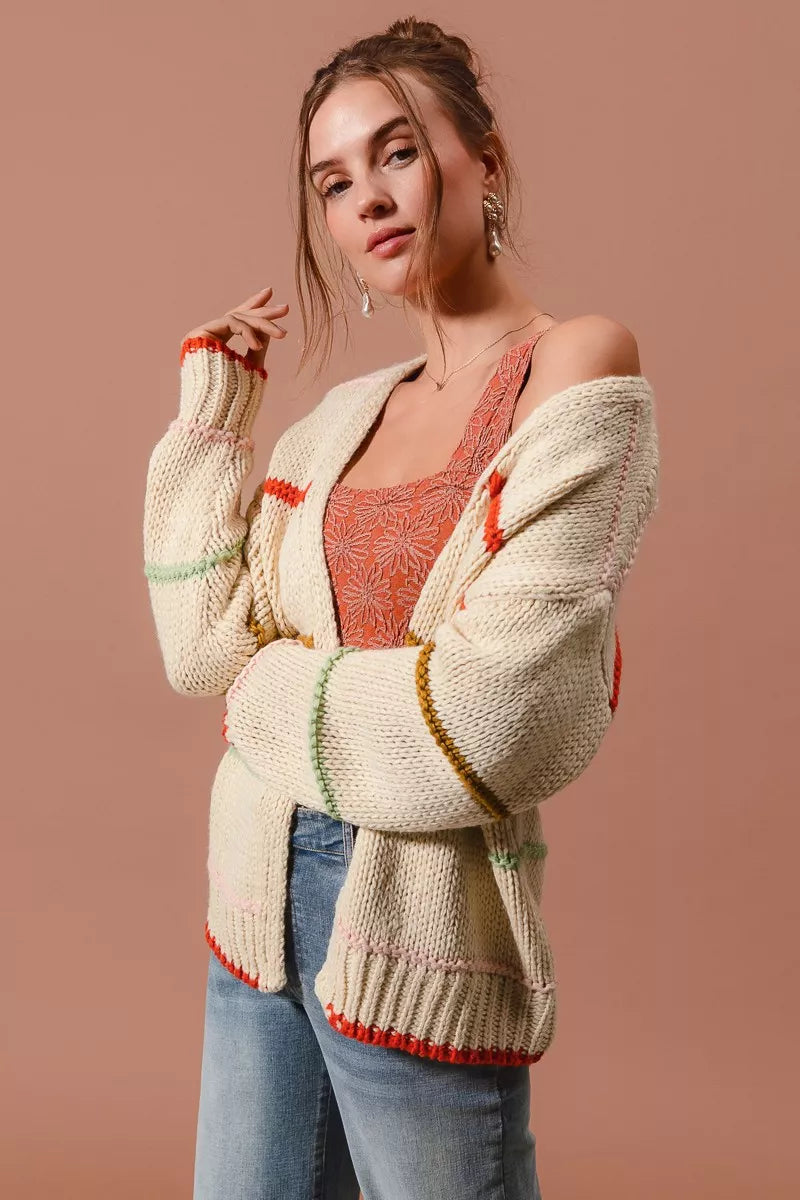 Woman wearing an oversized cream cardigan with multicolor stripe accents — cozy open knit sweater from A Whimsical Affair.