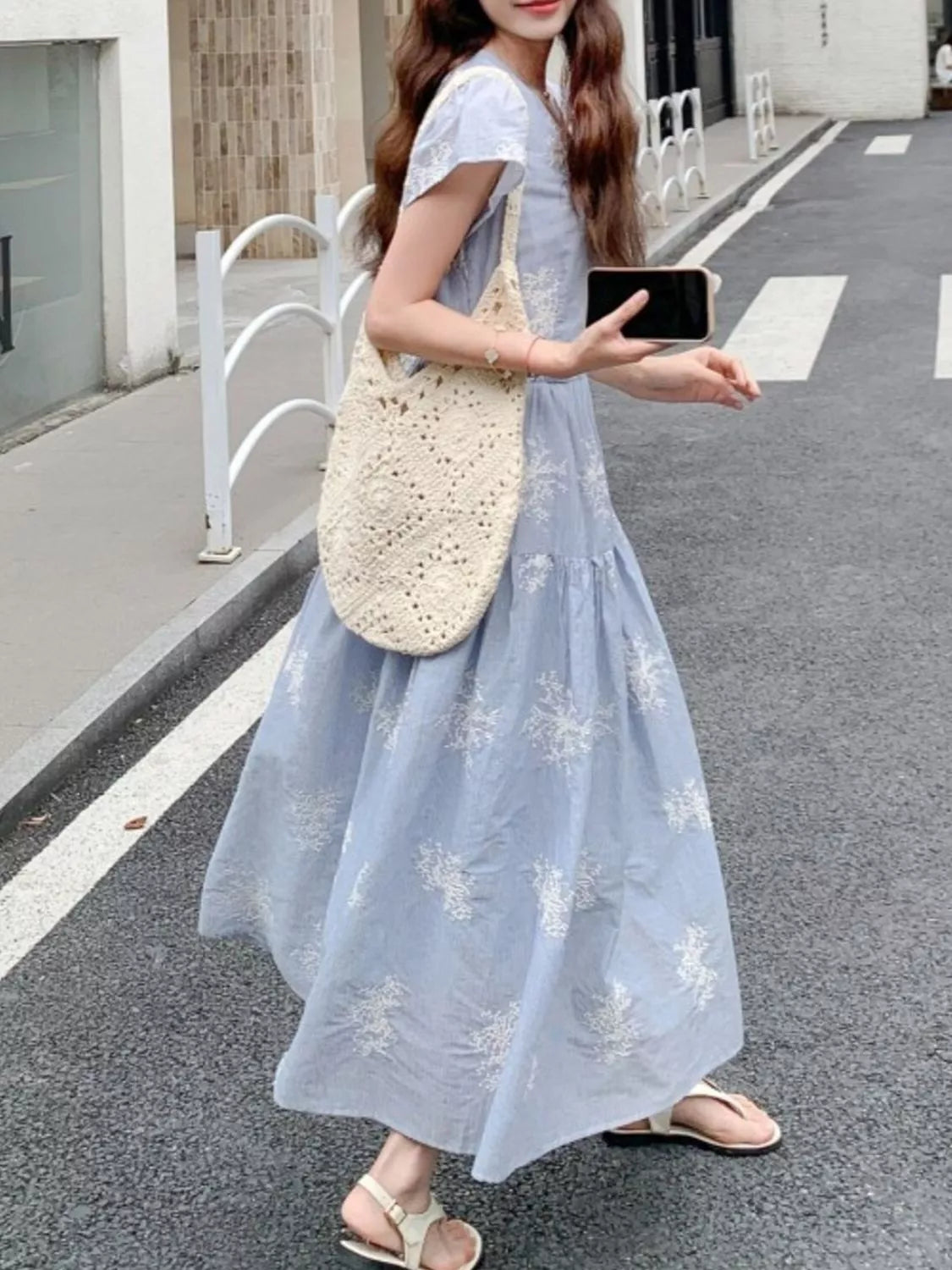 Model wearing the Whispering Bloom Buttoned Maxi Dress in light blue with white floral print, short sleeves, and a flowy tiered design.