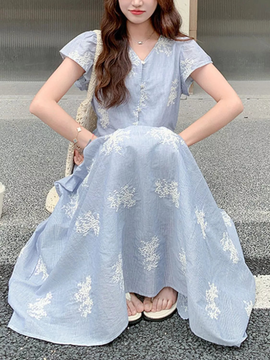 Model wearing the Whispering Bloom Buttoned Maxi Dress in light blue with white floral print, short sleeves, and a flowy tiered design.