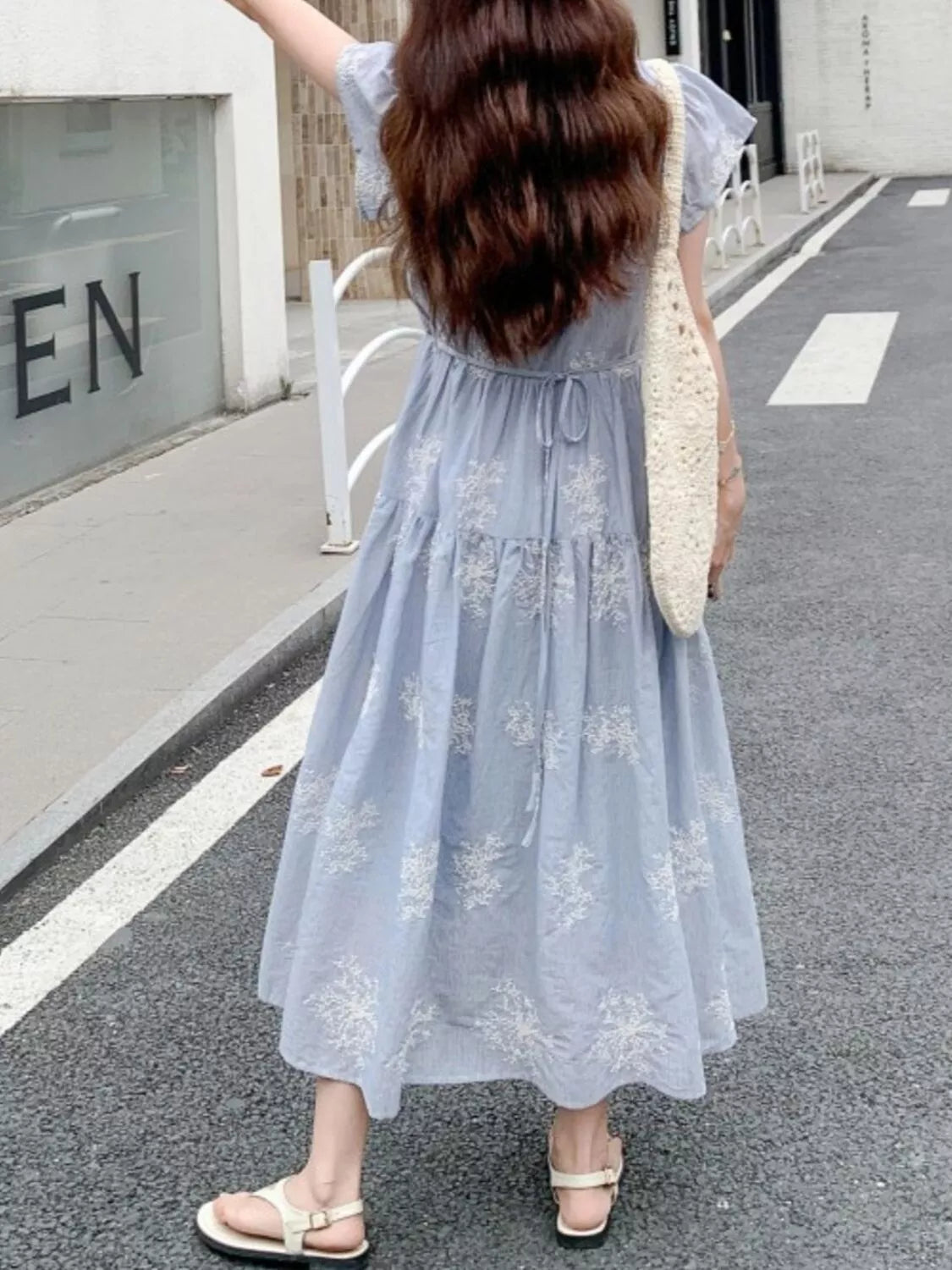 Model wearing the Whispering Bloom Buttoned Maxi Dress in light blue with white floral print, short sleeves, and a flowy tiered design.