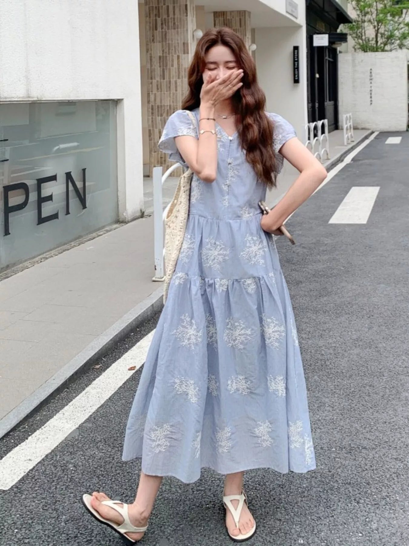 Model wearing the Whispering Bloom Buttoned Maxi Dress in light blue with white floral print, short sleeves, and a flowy tiered design.