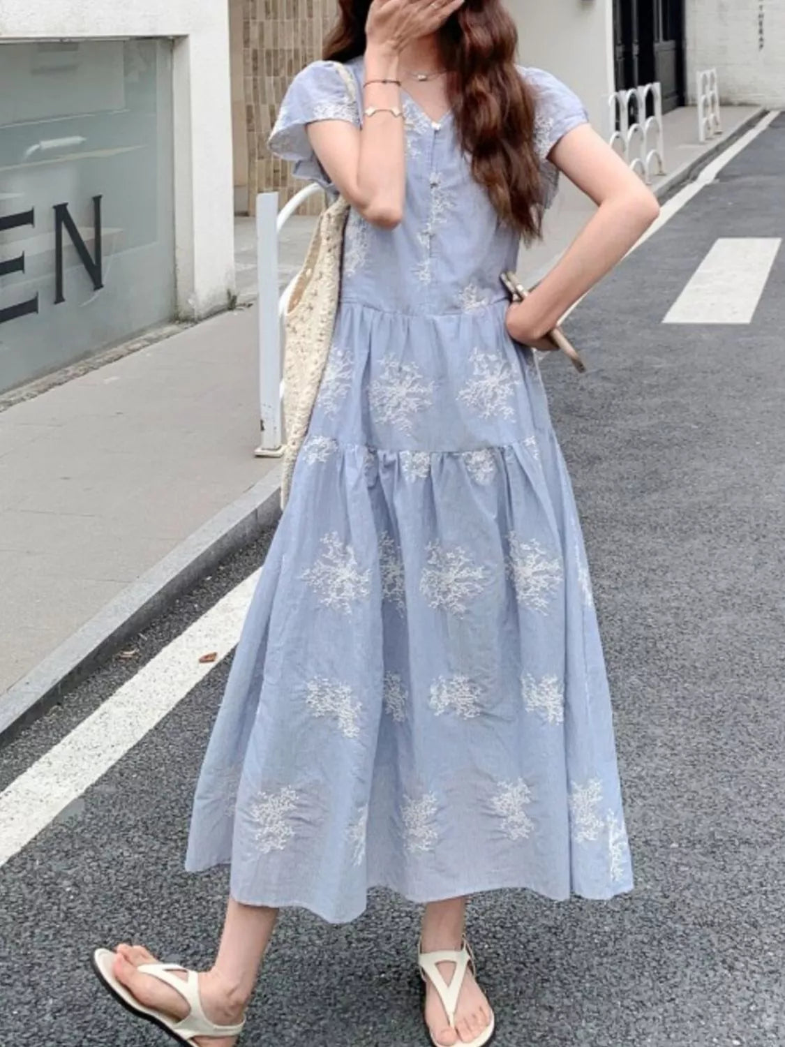 Model wearing the Whispering Bloom Buttoned Maxi Dress in light blue with white floral print, short sleeves, and a flowy tiered design.