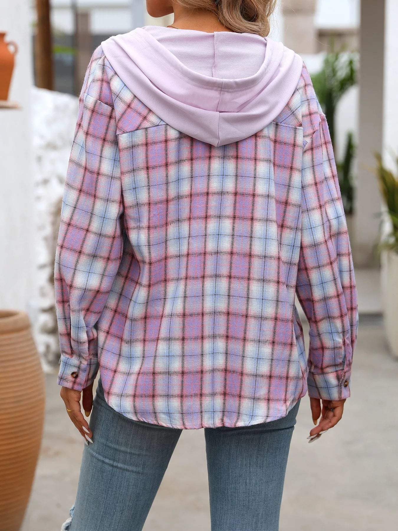Woman wearing a purple plaid button-up hoodie shirt layered over a white tank top with jeans and a tan bag, styled in a casual outdoor setting.