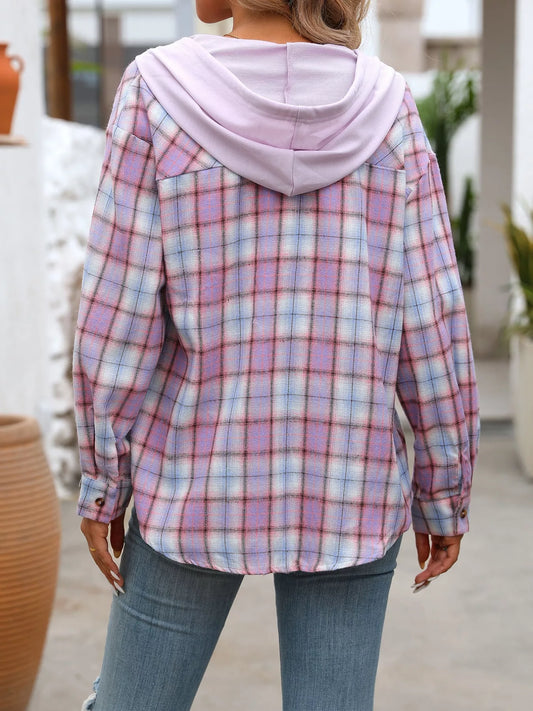 Woman wearing a purple plaid button-up hoodie shirt layered over a white tank top with jeans and a tan bag, styled in a casual outdoor setting.