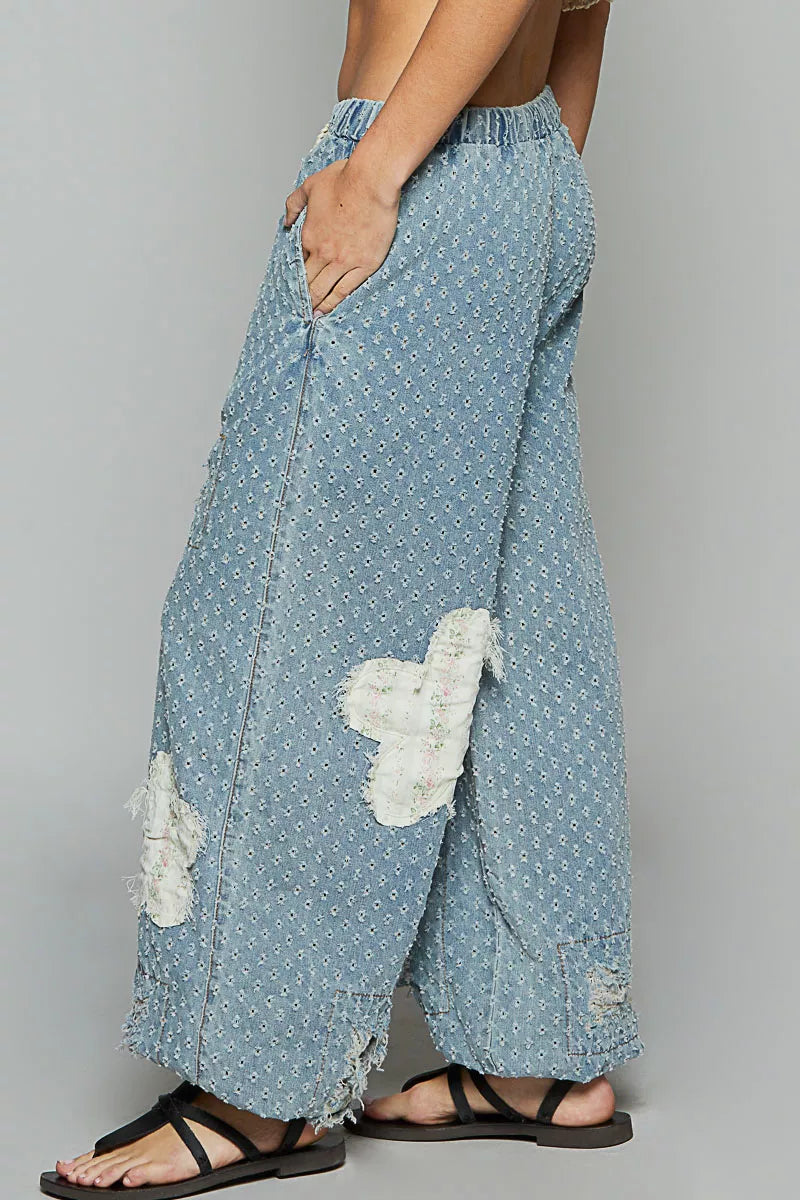 Vintage-washed blue joggers with floral appliqué patches, crochet distressing, and drawstring waist.