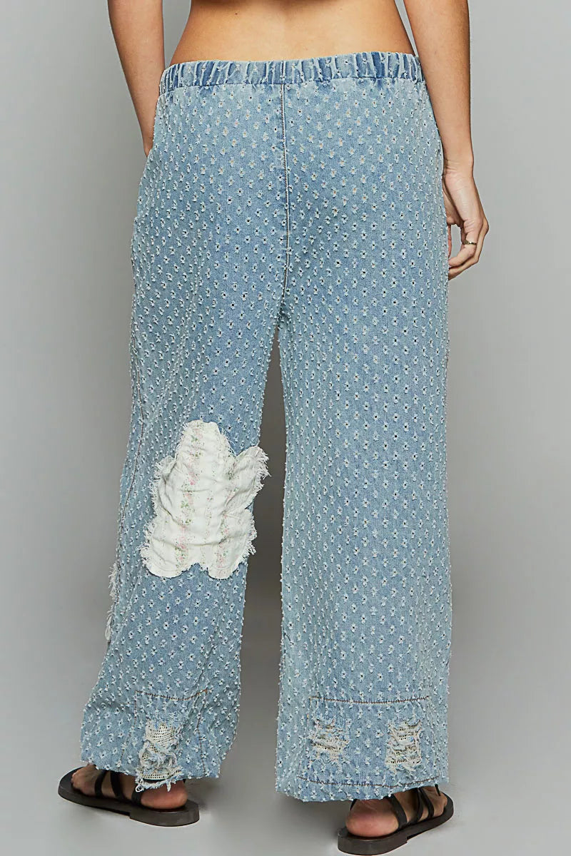 Vintage-washed blue joggers with floral appliqué patches, crochet distressing, and drawstring waist.