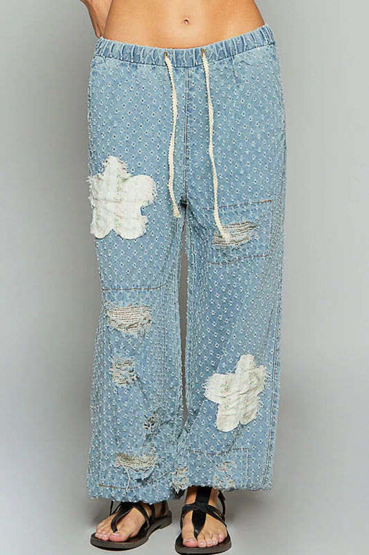 Vintage-washed blue joggers with floral appliqué patches, crochet distressing, and drawstring waist.