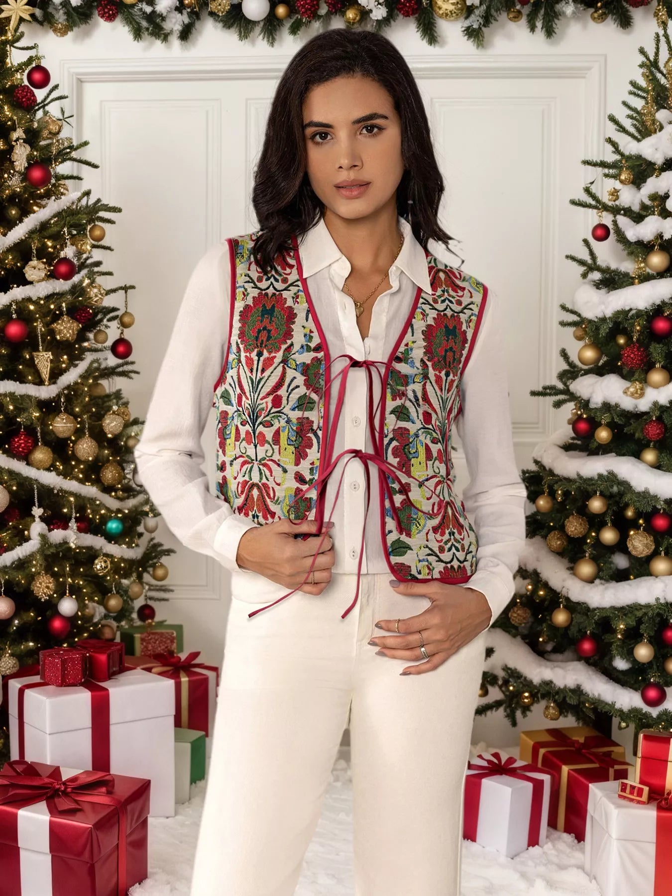 Embroidered floral tie-front vest layered over a white blouse, styled in a festive holiday setting with Christmas trees and presents.