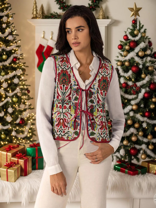 Embroidered floral tie-front vest layered over a white blouse, styled in a festive holiday setting with Christmas trees and presents.