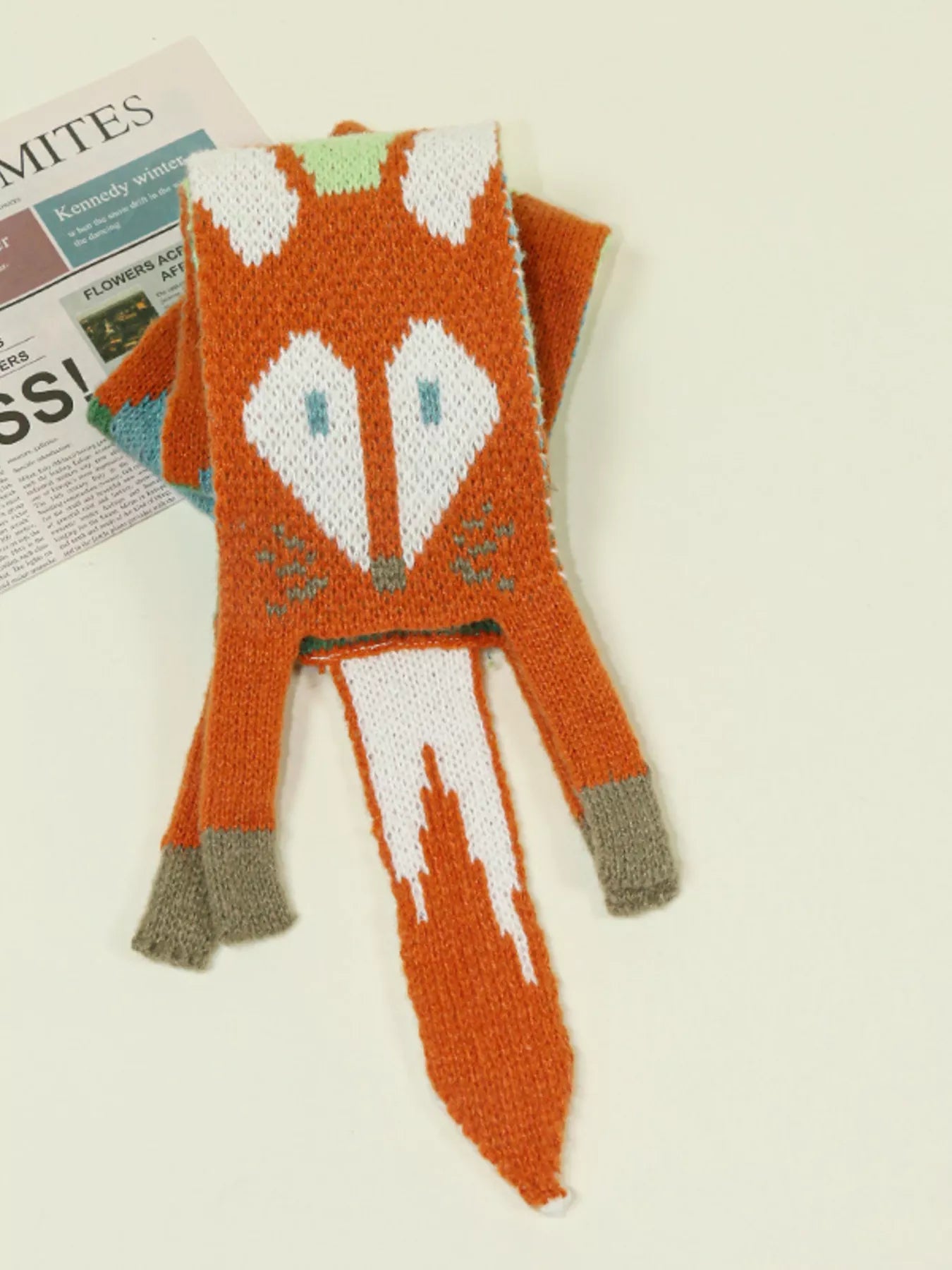 Whimsical knit fox scarf with soft texture and tapered ends hanging on a wooden branch.