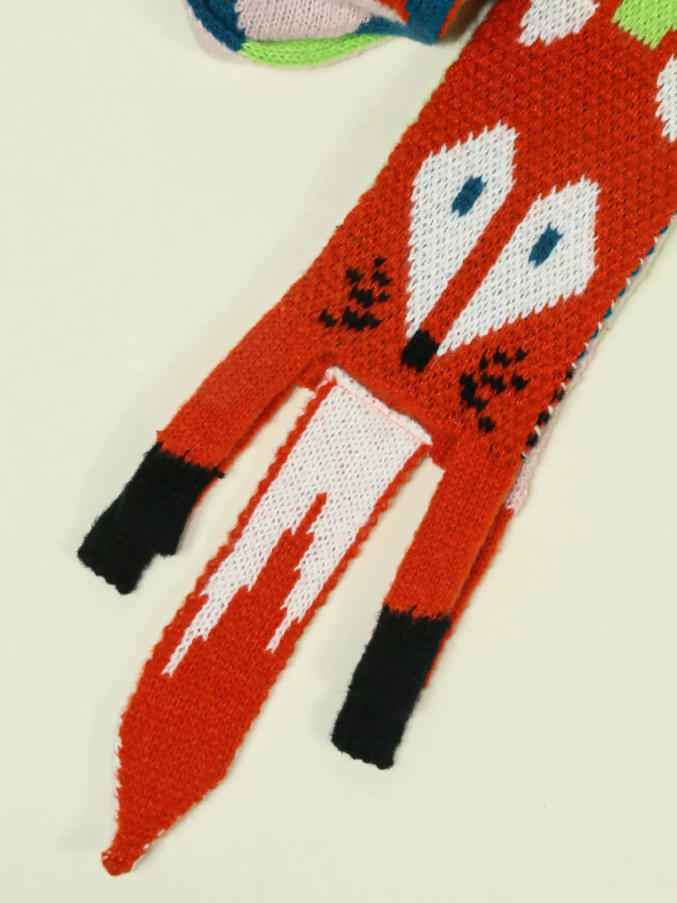Whimsical knit fox scarf with soft texture and tapered ends hanging on a wooden branch.