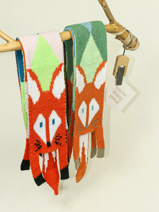 Whimsical knit fox scarf with soft texture and tapered ends hanging on a wooden branch.