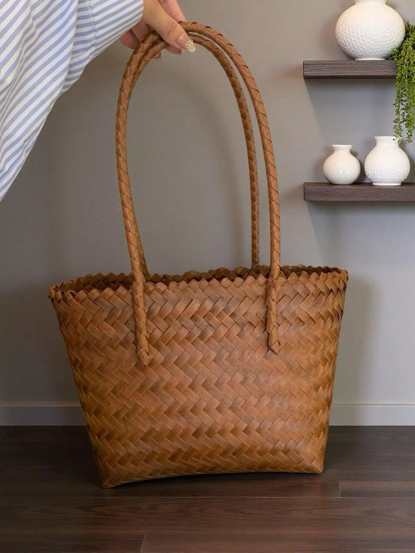 Medium woven brown tote bag with braided handles, displayed on a wooden surface beside a bowl of oranges and a lit candle.