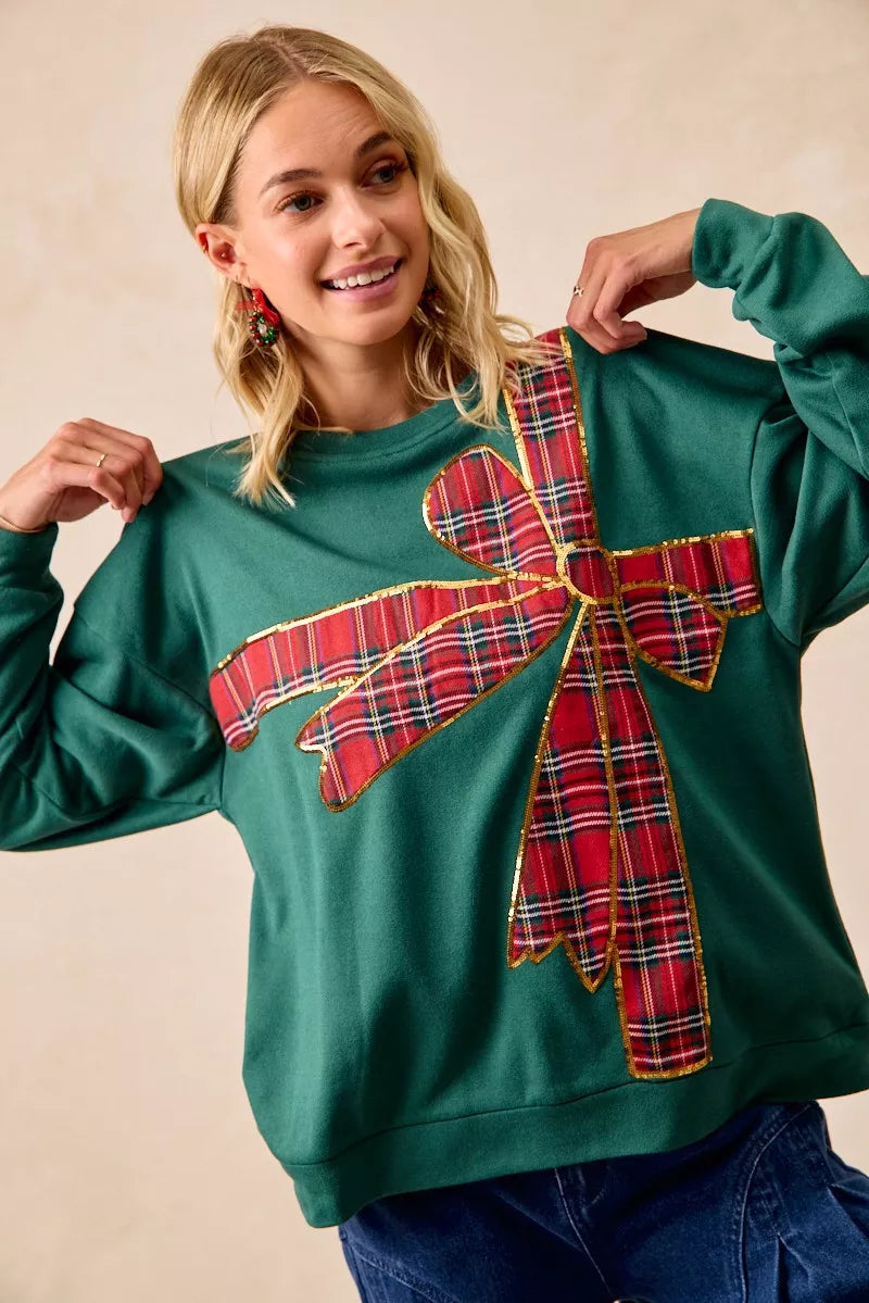 Woman wearing a green fleece pullover with a large red plaid bow design — festive holiday top from A Whimsical Affair.