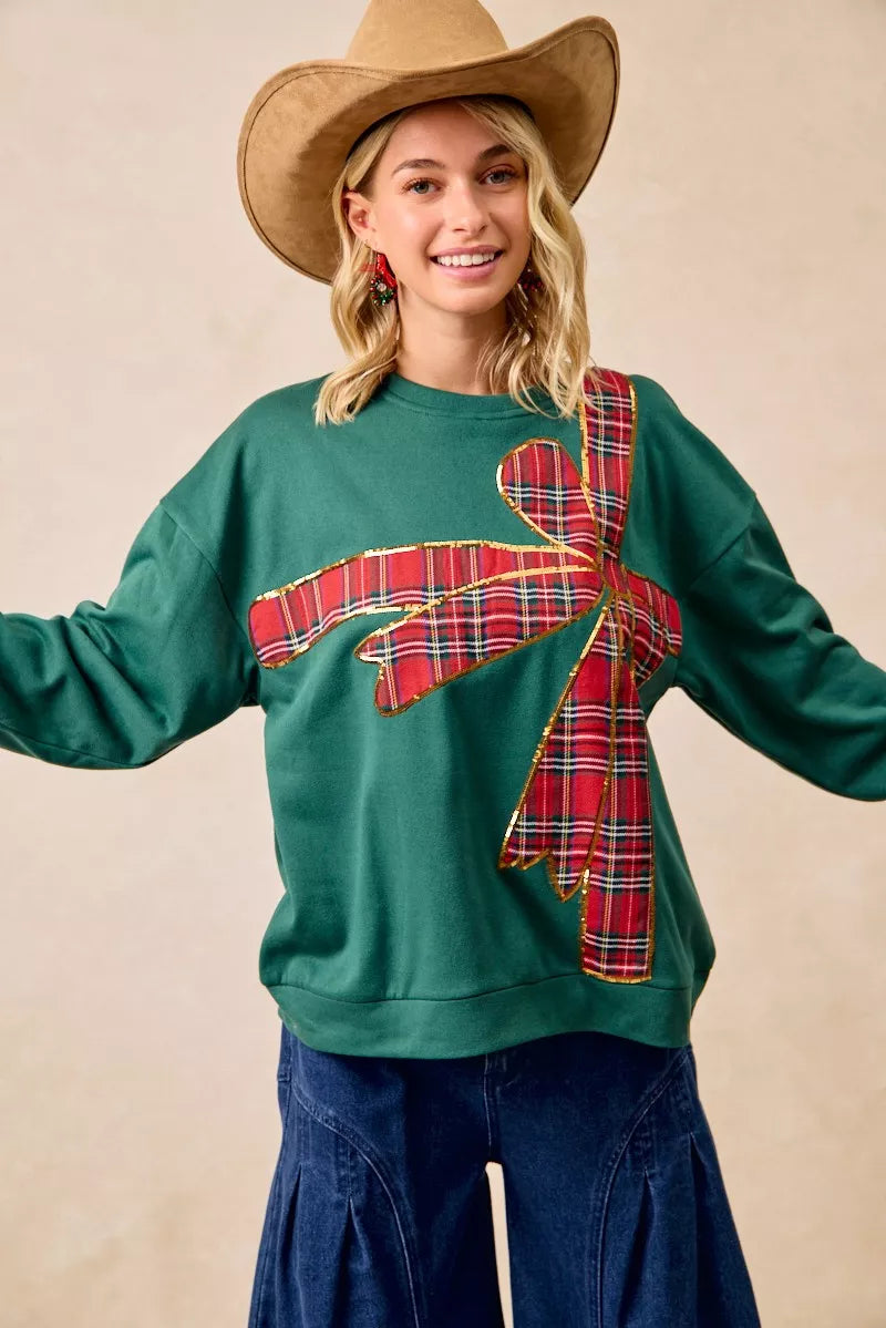 Woman wearing a green fleece pullover with a large red plaid bow design — festive holiday top from A Whimsical Affair.