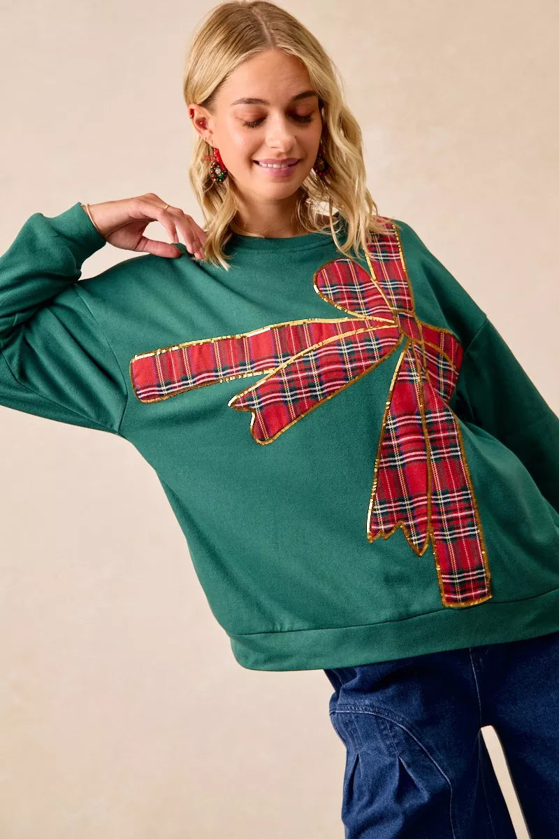 Woman wearing a green fleece pullover with a large red plaid bow design — festive holiday top from A Whimsical Affair.
