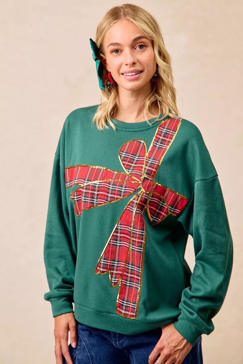 Woman wearing a green fleece pullover with a large red plaid bow design — festive holiday top from A Whimsical Affair.