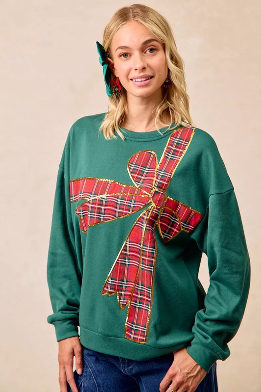 Woman wearing a green fleece pullover with a large red plaid bow design — festive holiday top from A Whimsical Affair.