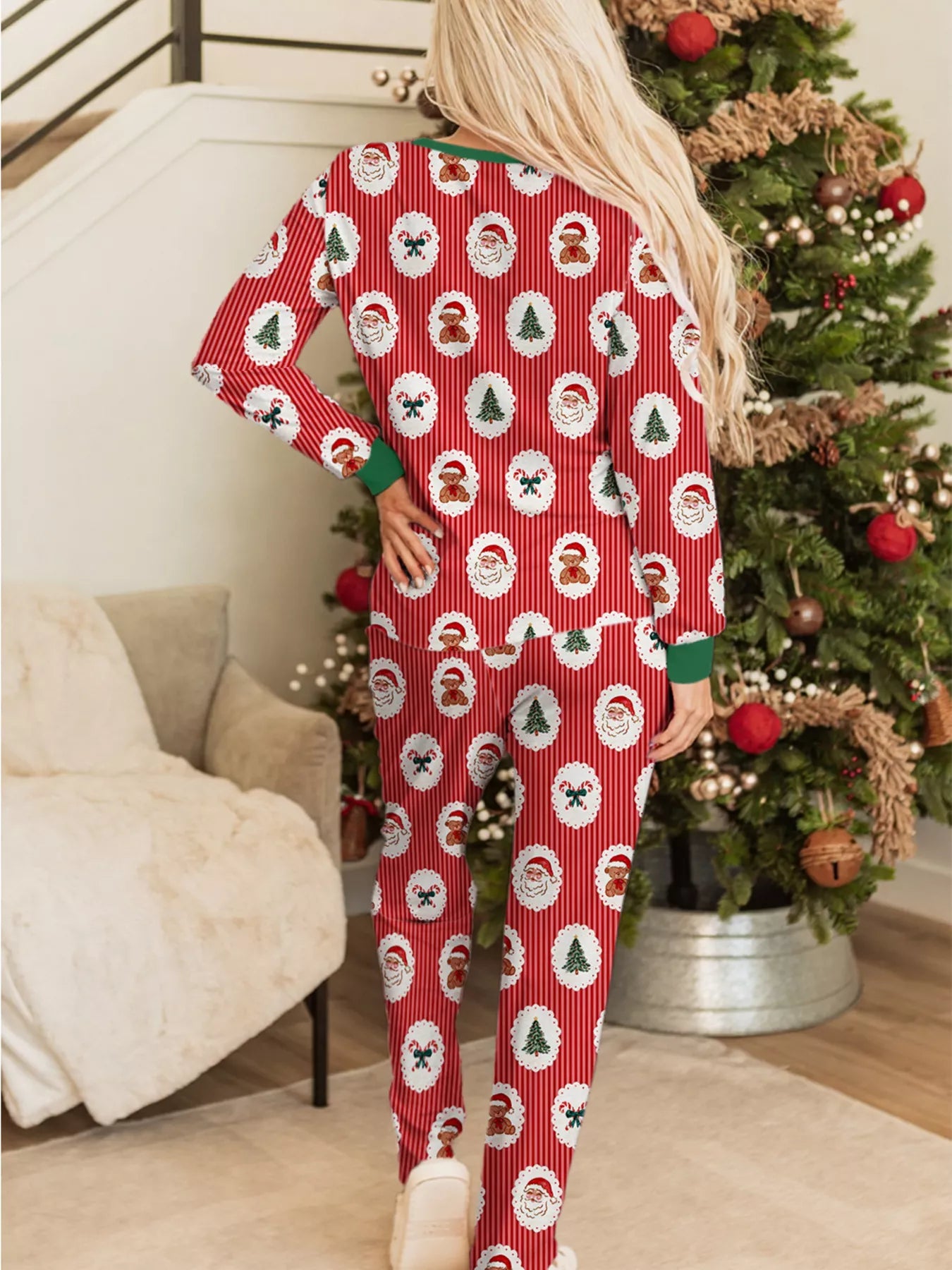 Red Christmas pajama set with Santa and tree prints, buttoned top, and drawstring pants worn beside a decorated Christmas tree.