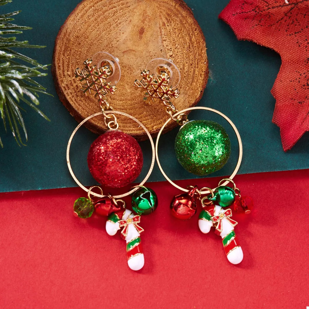 Gold snowflake holiday earrings with green and red glitter baubles, tiny bells, and candy-cane charms displayed on a red festive card.