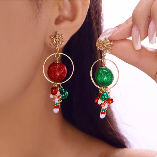 Gold snowflake holiday earrings with green and red glitter baubles, tiny bells, and candy-cane charms displayed on a red festive card.